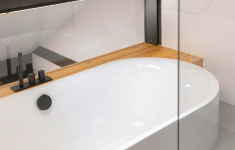 Millimetergenau eingelassene Badewanne auf Podest mit Holzverkleidung aus Echtholz mit schwarzen Armaturen für modernen Style und Stil mit natürlichem warmen Akzent